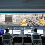 Operadores monitoram sistemas e painéis digitais em uma moderna sala de controle.
