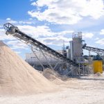 Planta moderna de processamento mineral com correias transportadoras sob céu azul.