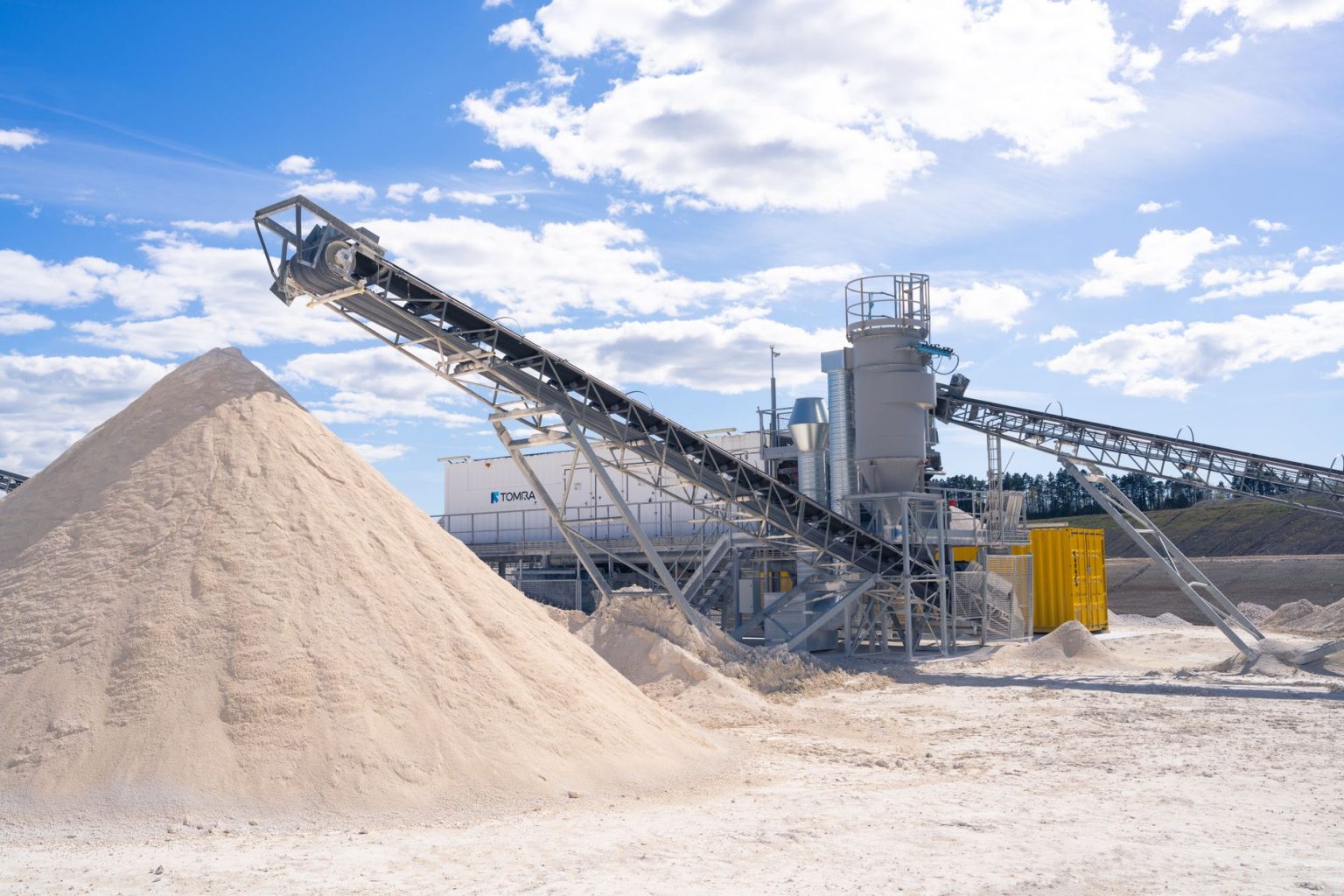 Planta moderna de processamento mineral com correias transportadoras sob céu azul.