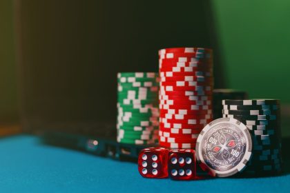Fichas de cassino e dados sobre uma mesa, ao lado de um laptop, remetendo às apostas online.