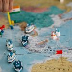 Mapa-múndi com miniaturas de navios e bandeiras indicando localidades e rotas de comércio internacional