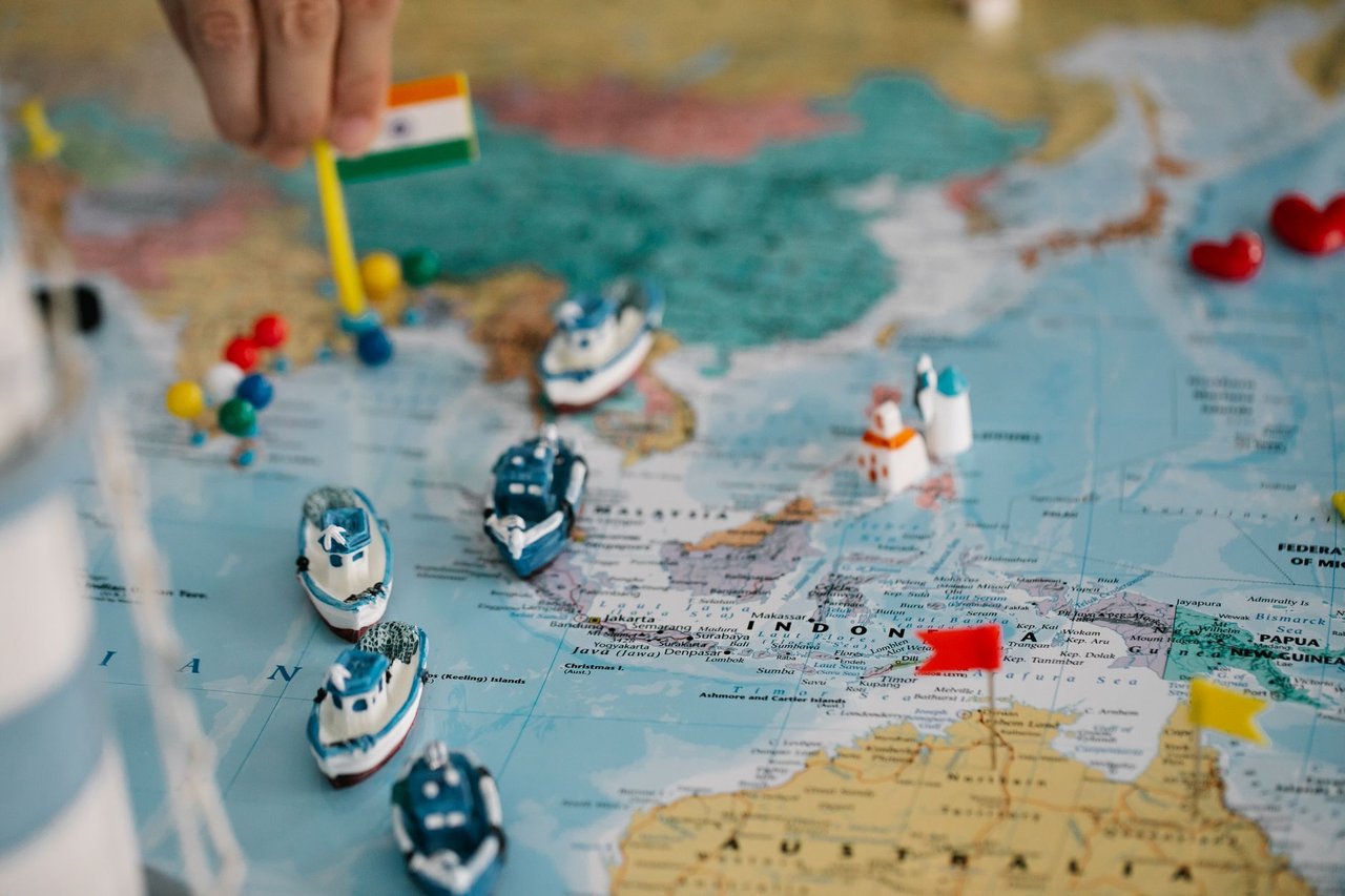 Mapa-múndi com miniaturas de navios e bandeiras indicando localidades e rotas de comércio internacional