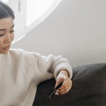 Mulher usa o celular e segura um cartão de crédito enquanto realiza uma compra online em casa.