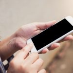 Pessoa usando um smartphone ao ar livre, com foco nas mãos e na tela do aparelho.