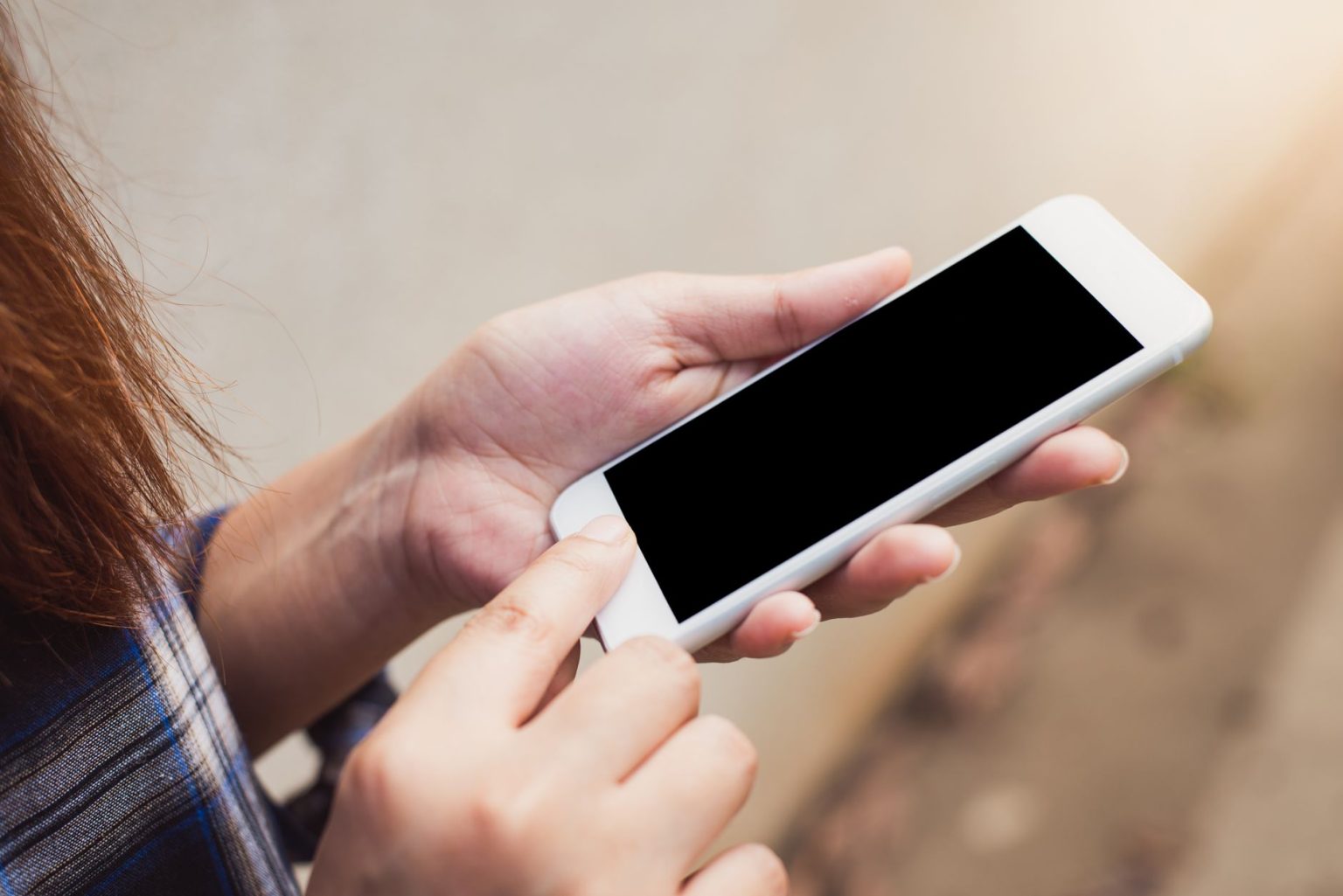 Pessoa usando um smartphone ao ar livre, com foco nas mãos e na tela do aparelho.
